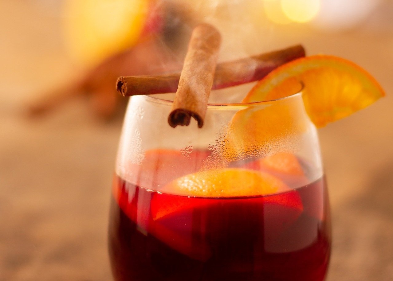 Das Bild zeigt Glühwein in einem Glas mit Zimt und Orangen.