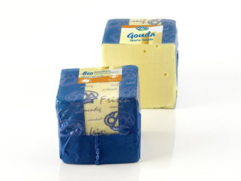 KI generiert: Das Bild zeigt zwei große Blöcke von Gouda-Käse, einer in blauer Verpackung und der andere teilweise ausgepackt. Der gezeigte Käse ist hellgelb und glatt, mit einigen kleinen Löchern.