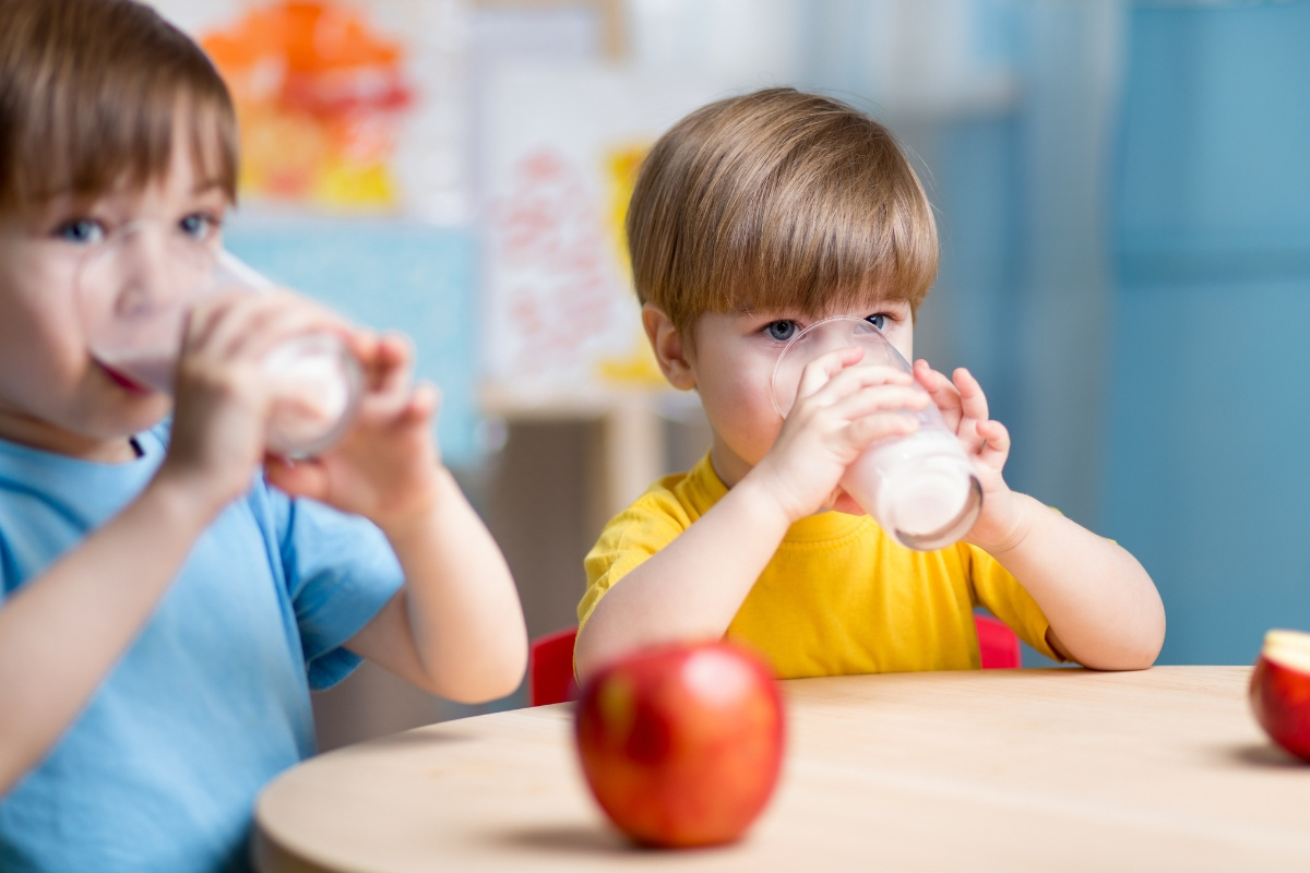 KI generiert: Zwei Kinder trinken Milch an einem Tisch mit einem roten Apfel im Vordergrund.